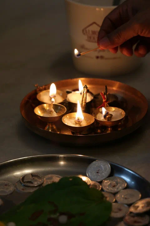 Five lit brass diyas arranged on a dark plate