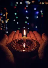 Hands holding a lit brass diya
