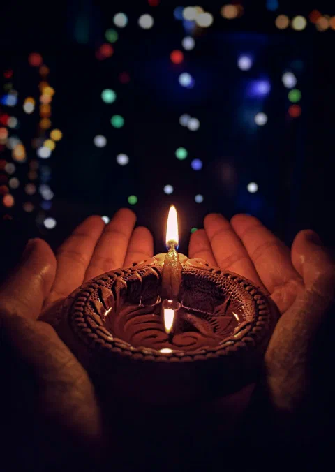Hands holding a lit brass diya
