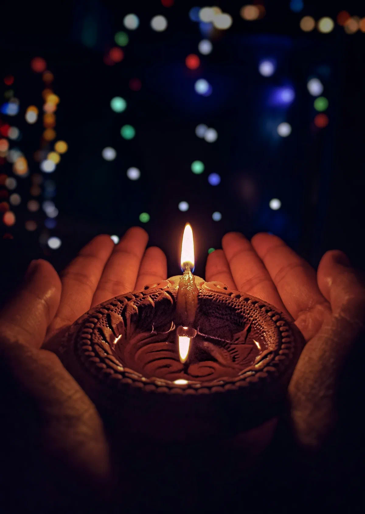Hands holding a lit brass diya