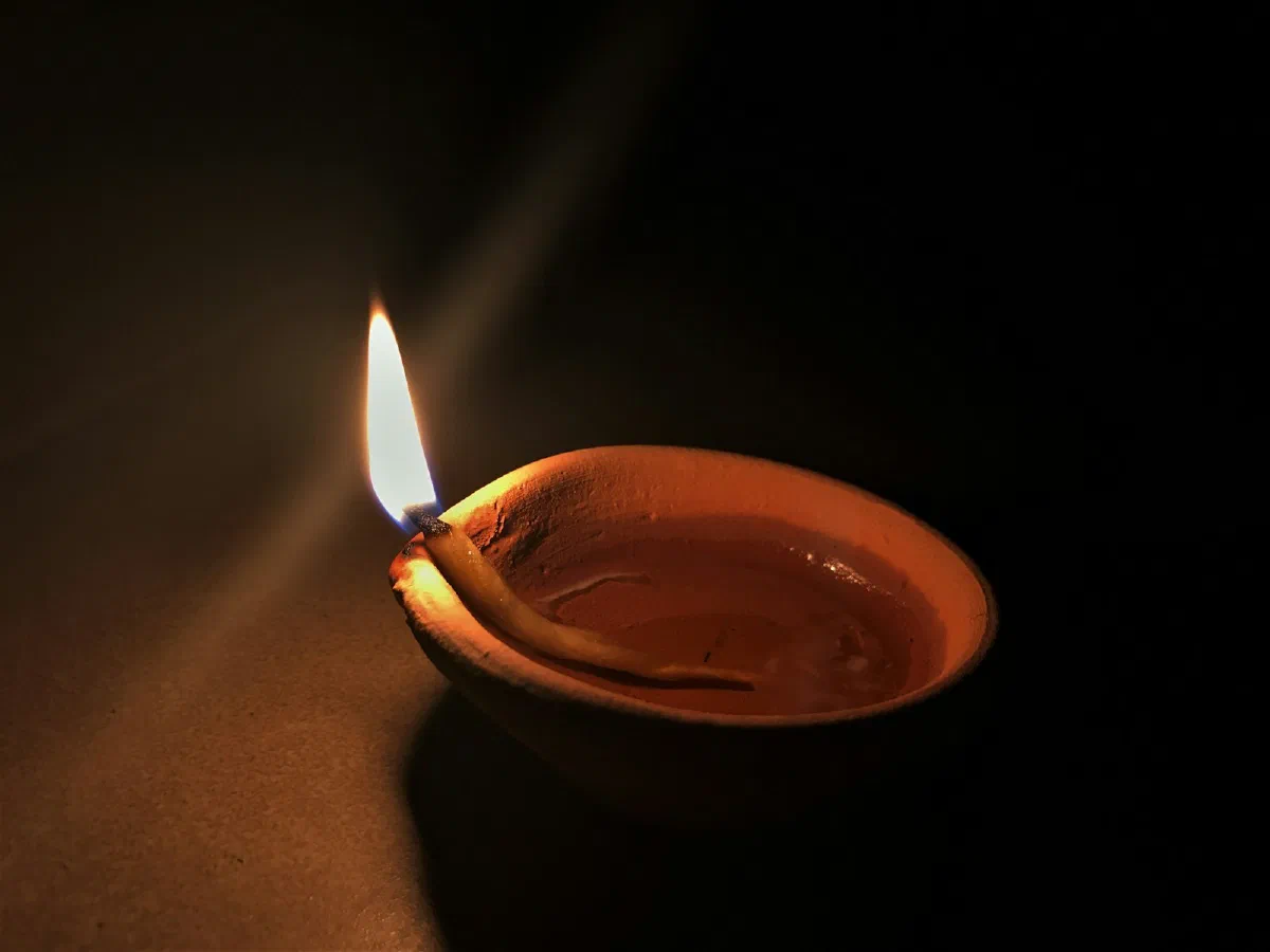 A single brass diya burning on a dark surface