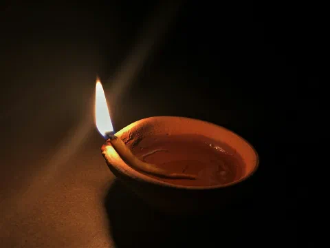 A single brass diya burning on a dark surface